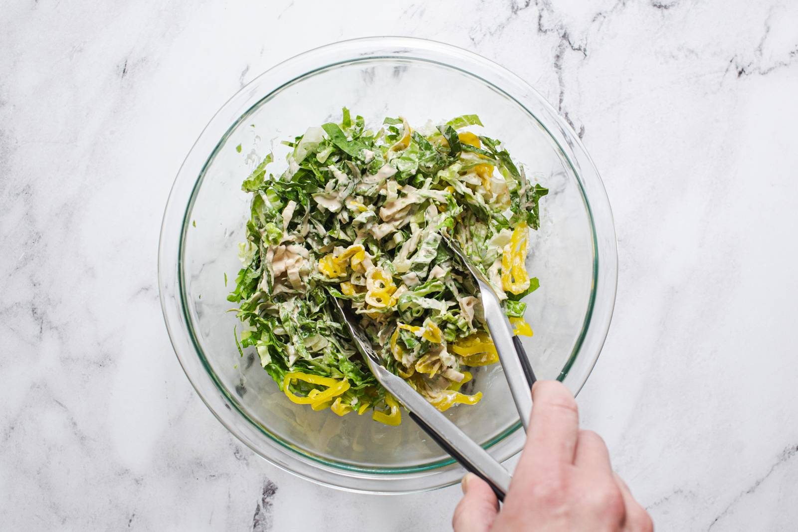 Tossing caesar salad in a bowl.