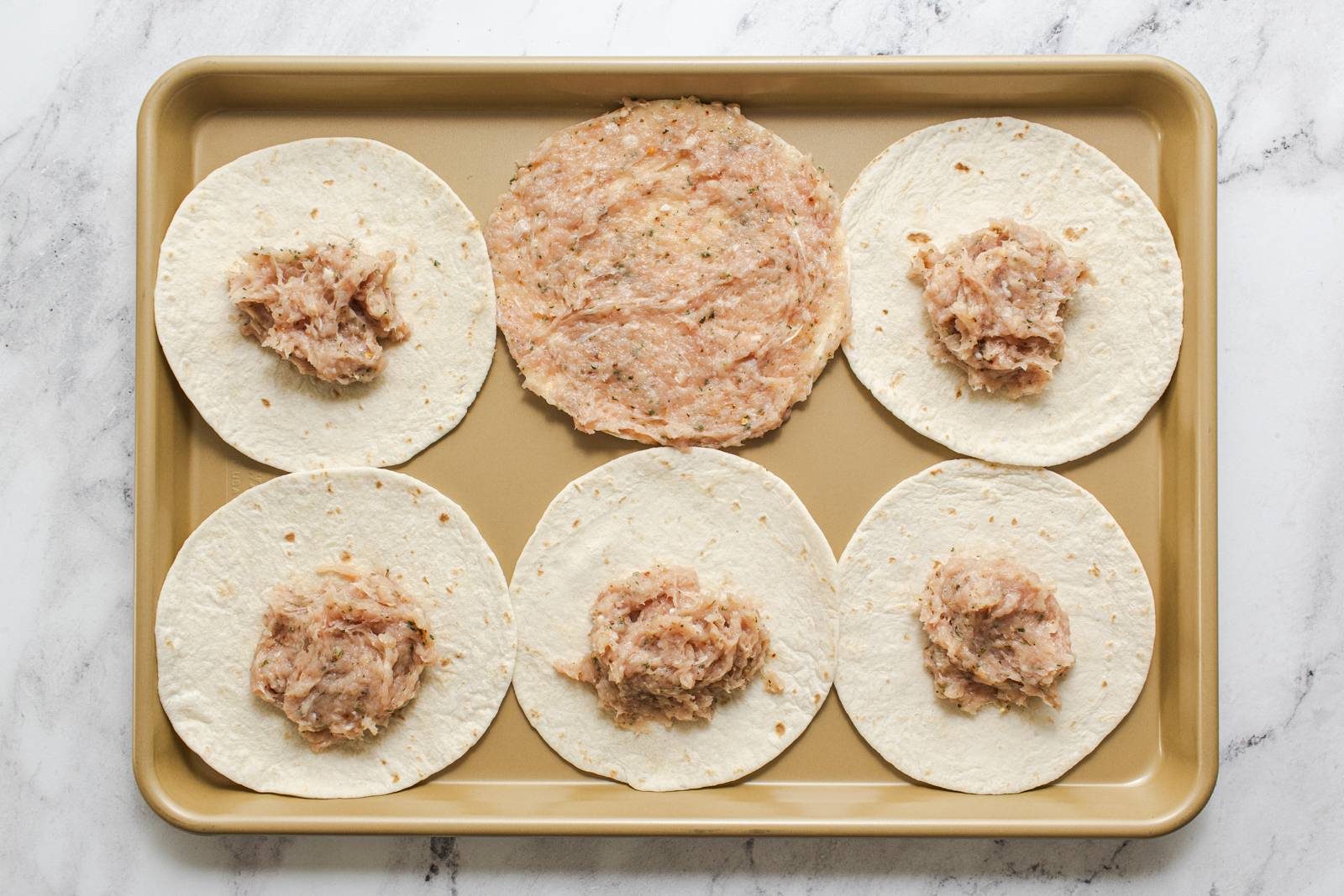 Spreading ground chicken mixture on tortillas.