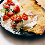 Socca with Whipped Feta and Tomato Salad on a plate.